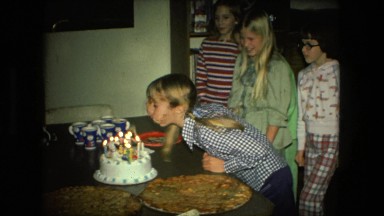 1974: cute young girl with pigtails blowing out birthday candles on cake