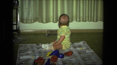 1974: baby sitting on blanket in middle of room sucking thumb learning ways