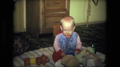1974: happy child sits on blanket surrounded by many toys tries to decide which