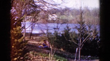 1960: man works the land while river flows behind him, his house