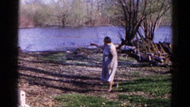 1960: Woman Explores Lakeside Area with Grass and Trees Surrounding Her