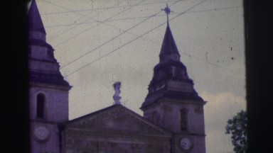1967: magnificent church with two towers near to road with vehicles moving