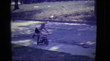 1946: cute caucasian blond kid riding scooter on sidewalk coming up to house