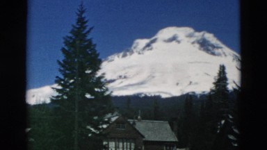 1958: snow covered mountain peak view with wooden house and coniferous forest