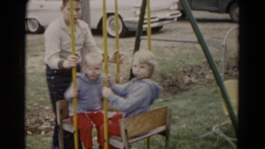 1962: young boy pushing two toddler aged girls on swing set swing in yard