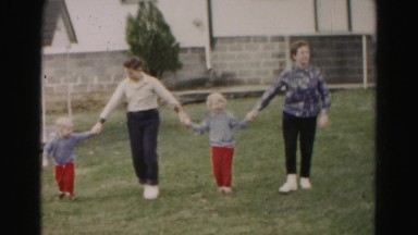 1962: family holding hands playing in the freshly mowed grass frontyard