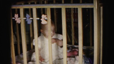 1962: caregiver hands toy to baby sitting in crib playing in safe environment