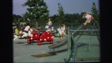 1972: many children are at playground playing on equipment such as teeter totter