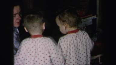 1972: two toddlers in matching pajamas looking at new toys with mother helping