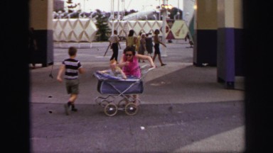 1972: Woman at Amusement Park Struggling to Keep Child in Stroller