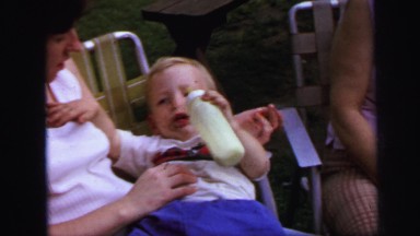 1972: woman holding toddler in her lap as he drinks from bottle LYNBROOK
