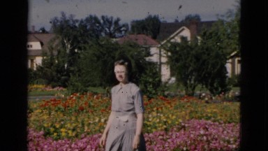 1952: a lady wearing a hat is walking in front of flowers