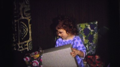 1974: a little girl in pajamas opening the wrapping on a christmas gift CAMDEN