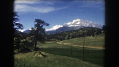 1962: Green Grass, Trees, and Snow-Covered Mountains Seen