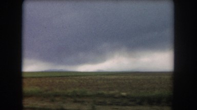 1962: view from a moving vehicle along a flat landscape with a storm approaching