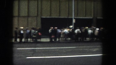 1962: middle-age shoppers line downtown block awaiting unknown event in the 60s