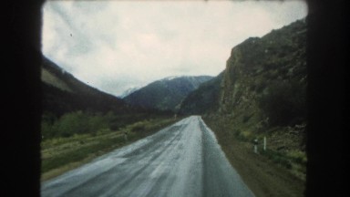 1962: Front View of Vehicle Touring Narrow Wet Road Through Algerian Countryside