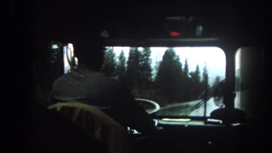 1962: Bespectacled Man Guides Bus Down Pine-Lined Mountain Road in Colorado