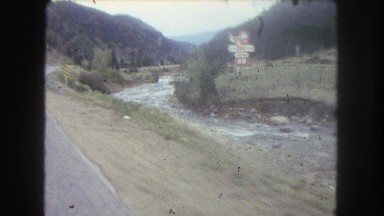 1962: vehicle on the road passing by a lake, trees and relieves COLORADO