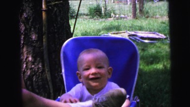 1964: baby is happy playing with a person's foot sitting in his chair at a park