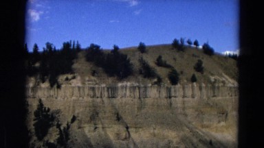 1967: Woman Posing at Yellowstone National Park Entrance with Mountain Ridge and Canyon View