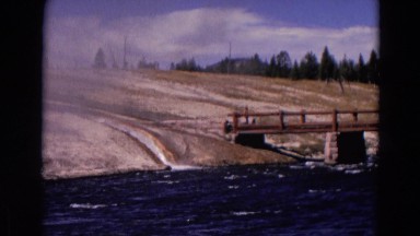1967: water is falling over the rock to the blue water body with a bridge