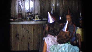 1961: a woman setting a birthday cake with lighted candles on a table