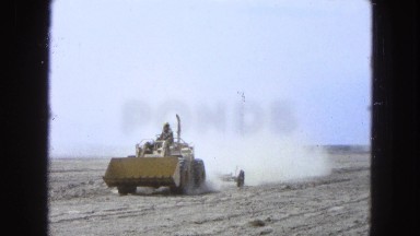 1965: Workman Driving a Backhoe on a Dusty Road in a Deserted Area of Mexico