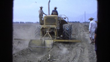 1965: a man driving a large backhoe to make a ditch as men walk along the side