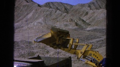 1965: an excavator throwing dirt in a truck is in a sand-filled and dry place.