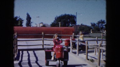 1961: two girls driving two mechanical toy tractors on structures with wood