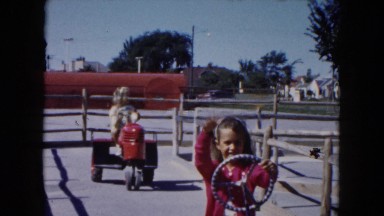 1961: Two Girls Driving Tractors and Waving at Camera in Michigan