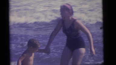 1964: a woman holding a little boy's hand while fighting the ocean's surf