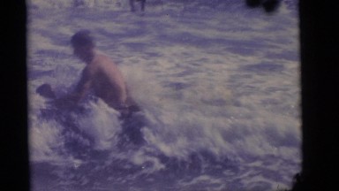 1964: father playing in the ocean with his son while the boy kicks his feet