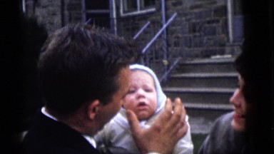 1964: a man is holding a baby and a woman is standing next to him smiling