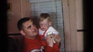 1964: father is holding his toddler son and cleaning his hand with a napkin