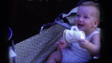 1964: happy baby boy plays with paper cup at young girl's birthday party CAMDEN