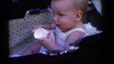 1964: a laughing toddler is in a baby carriage while playing with a cup CAMDEN
