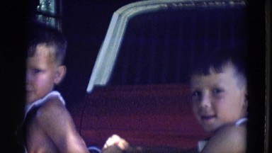 1963: Two Small Boys Wearing Bibs Sitting in Truck Bed Waving, Lincoln, Nebraska