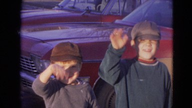 1963: two young boys in hats standing outdoor in front of a car waving LINCOLN