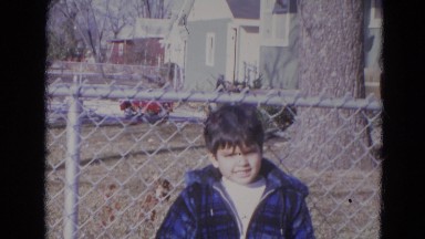 1963: a young boy in a coat standing in front of a chain-link fence LINCOLN