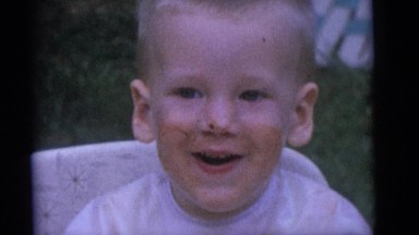 1964: blonde baby laughing with food on his face, surrounded by family