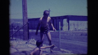 1968: two young boys playing in a muddy, water filled hole in the ground.