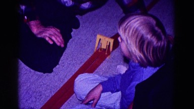 1968: an older man assists a child while assembling a train track