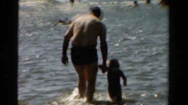 1954: a father is teaching his kid to walk in the ocean or the sea OHIO