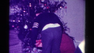 1954: a woman is reading names on christmas presents and handing them to a boy