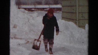 1954: a child is shoveling piles of heavy white snow on a very cold winter day