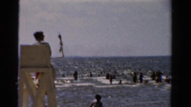 1954: a handsome lifeguard in a chair overlooking swimmers in the ocean NEW YORK