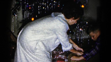 1959: a woman helps a boy open a christmas present and pull it out of its box