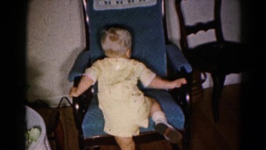 1959: little boy in a yellow jumpsuit is trying to climb into a blue chair